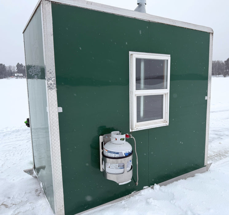 A green ice fishing house with a propane tank holder mounted to the side with a propane tank inside it