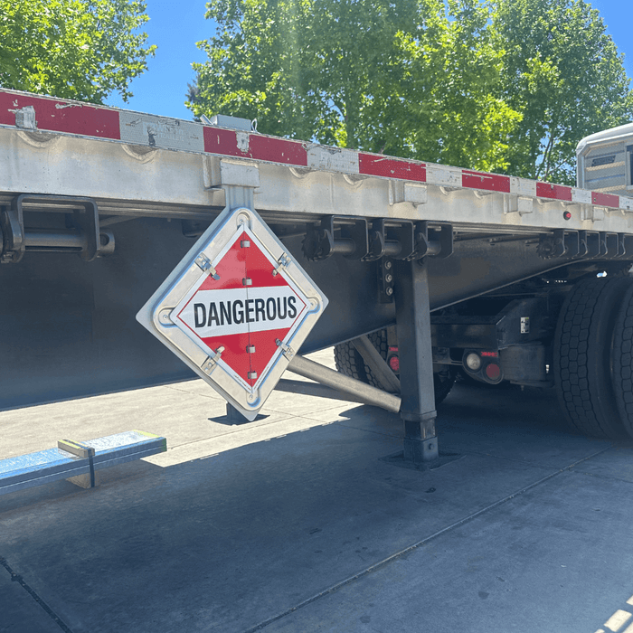 A flatbed semi trailer with a hazmat placard holder mounted with a sign saying "Dangerous"